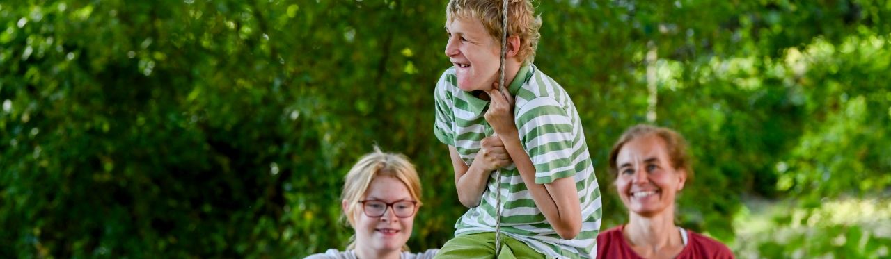 3 Kinder im Garten, eins davon hält sich am Seil fest